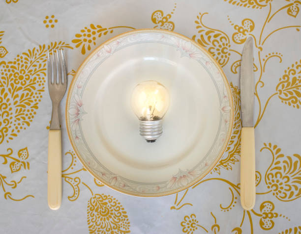 istock Knife and fork on a table, with a lit light bulb lamp in a porcelain plate 822162848