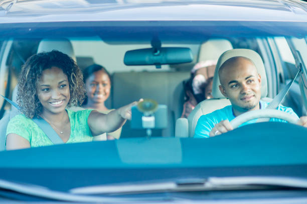 Driving In A Van A mother, father, and two sisters of African descent are in a van during a road trip. They are wearing casual clothing. The father is driving and the mother is pointing at something. family-van-driving stock pictures, royalty-free photos & images