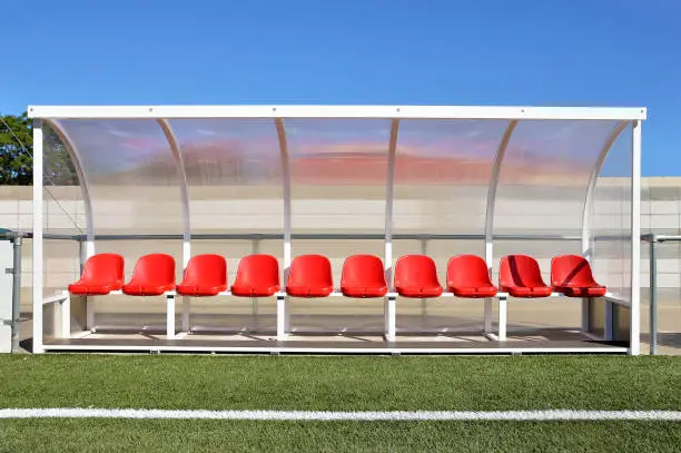 sport bench with red plastic seats in the stadium players outdoors with red paint under transparent plastic roof as banking players