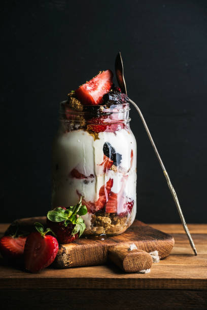 jogurt granola owsiana z truskawkami, morwą, miodem i liśćmi mięty w wysokim szklanym słoiku na czarnym tle - jar oatmeal granola glass zdjęcia i obrazy z banku zdjęć