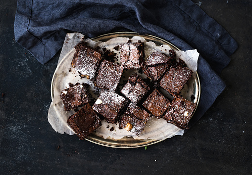 Dark chocolate and walnut brownie squares on a silver tray over black grunge surface, horizontal