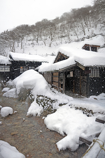 Small japanese village in winter, river flows, tradiotional old houses, big snowdrifts, hill with forest, thermal spring, Akita, Japan