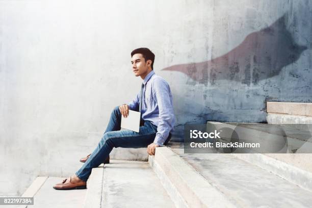 Power Success And Leadership In Business Concept Young Man Sitting On Office Outdoor Stair And Looking Forward With Superhero Blanket Shadow Shade On The Wall Side View Stock Photo - Download Image Now