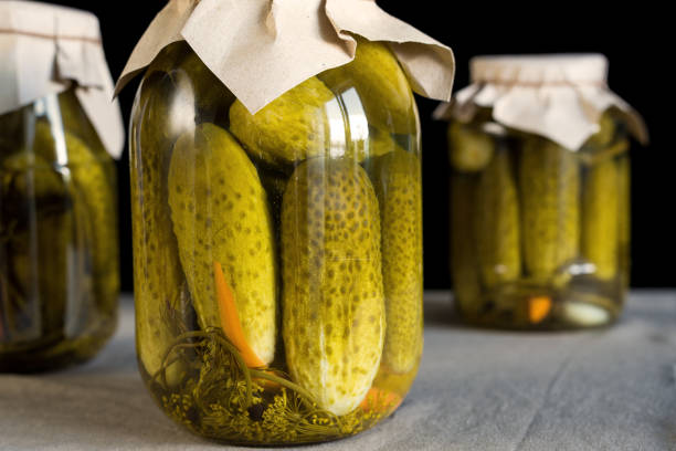 Closed glass transparent jar with fresh pickled cucumbers on black background, homemade preserved vegetables.
