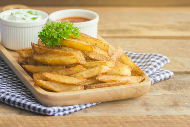 homemade french fries serve with ketchup and sour cream or mayonnaise. golden brown crispy french fries sprinkle with salt and oregano on wood plate for snack or appetizer. french fries on wood table. - oregano freshness herb brown imagens e fotografias de stock