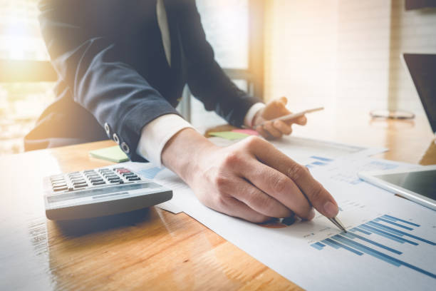 istock Close up business man holding pen and point to data sheet while using smartphone and calculator for financial, tax, account in his office 822294506