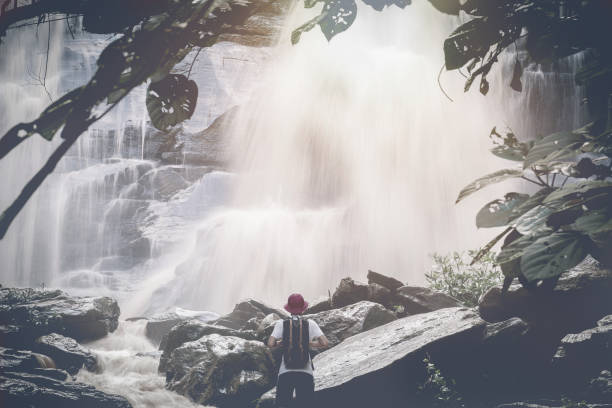 istock Traveler with backpack standing in front of waterfall waterfall view.  tropical vacation concept with vintage filter effect 822297236