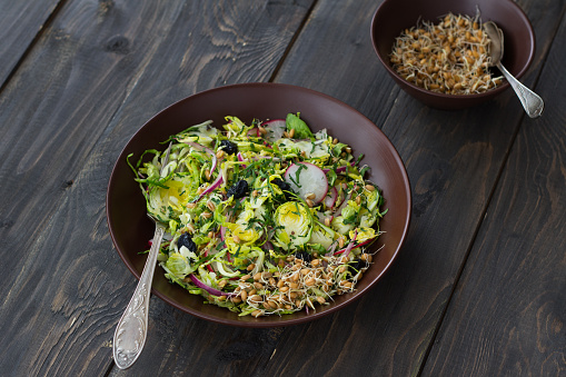 Salad from brussels sprouts with radish, raisins and sprouts of wheat. Healthy diet detox food. On a wooden background in a rustic style