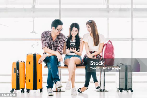 Group Of Young Asian Travelers Using Smartphone Checking Flight Or Online Checkin At Airport Together With Luggage Travel Abroad Summer Holiday Trip Or Mobile Phone Application Technology Concept Stock Photo - Download Image Now