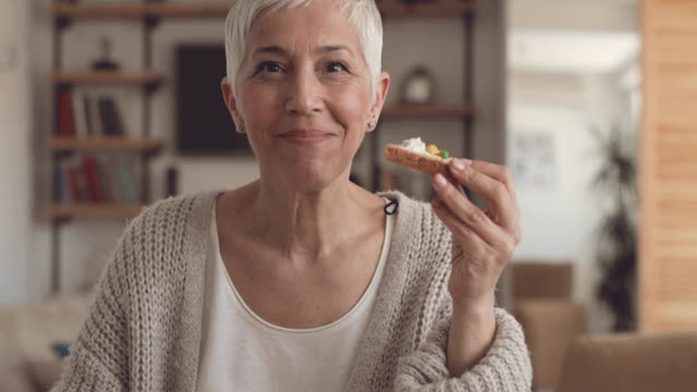Happy mature woman having a breakfast at home and showing thumbs up while looking at camera.