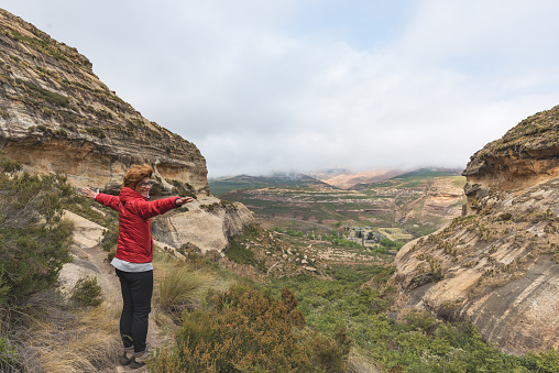 Tourist standing with outstretched arms and looking at the panoramic view in the majestic Golden Gate Highlands National Park, travel destination in South Africa. Concept of adventure and traveling people.