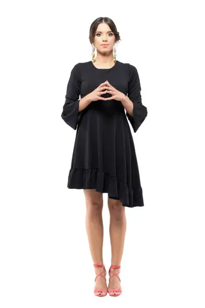Formal woman in black dress looking at camera with touching fingertips steeple gesture. Full body length portrait isolated on white background.