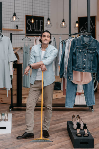 istock smiling young man holding broom while sweeping floor in boutique 822419678