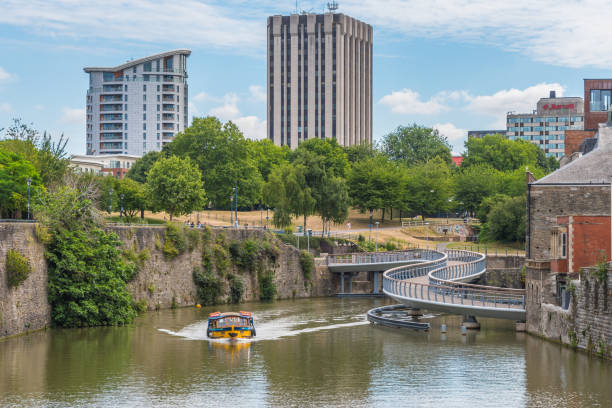 Bristol, UK - 4th August 2016: Moored canal boats and modern office blocks along The Floating Harbour and Temple Back (Temple Quay) regeneration business area in central Bristol City, UK. Workers leave their workplaces during a sunny summertime lunch break.