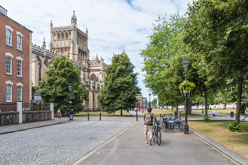 A man pushes a bicycle along a road near Bristol Cathedral on a sunny day.