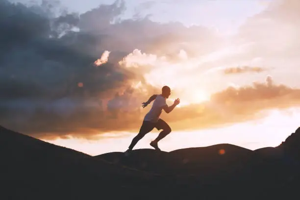 Photo of Athlete runs quickly through the hills outdoors at sunset. Healthy lifestyle concept