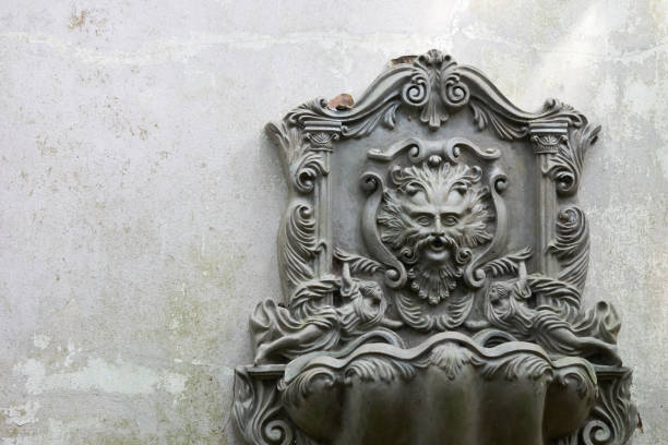 istock Old Lion Head Fountain, which is mounted on a white-gray wall. Which is not used for a long time, do leaves covered. See the whole garden. copy space 822579406