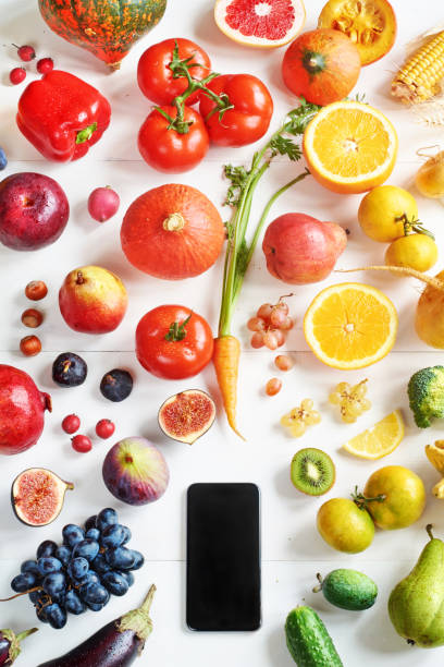 istock Rainbow colored fruits and vegetables on a white table and a cellphone. 822586376