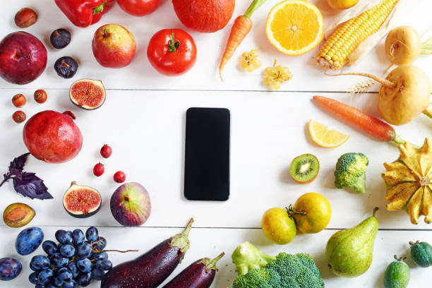 istock Rainbow colored fruits and vegetables on a white table and a cellphone. 822586756