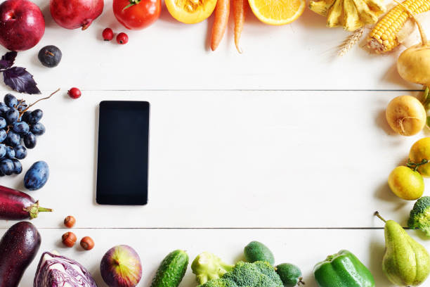istock Rainbow colored fruits and vegetables and cellphone on a white table with copy space. 822591654