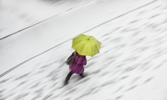 Woman with green umbrella walking in snowstorm. Blurred motion - view from above.