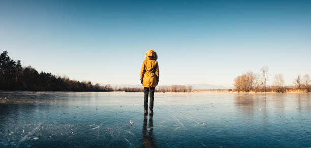 Woman with orange jacket standing on a frozen lake.