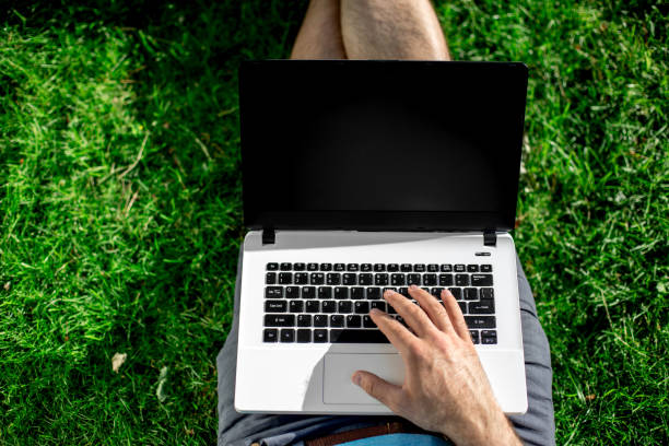 istock Cropped shot of man using laptop with blank screen while sitting on green grass 822623518
