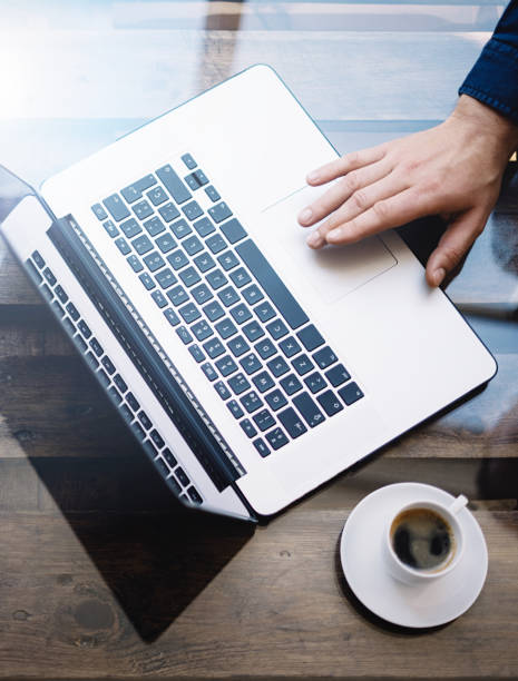 istock Man working with laptop at sunny office.Male hand pointing on notebook trackpad.Modern notebook, cup of black coffee on the wooden table.Reflections on glass surface.Vertical.Top view. 822687892