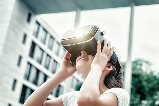 smiling teenage girl with virtual reality simulator looking up outdoors