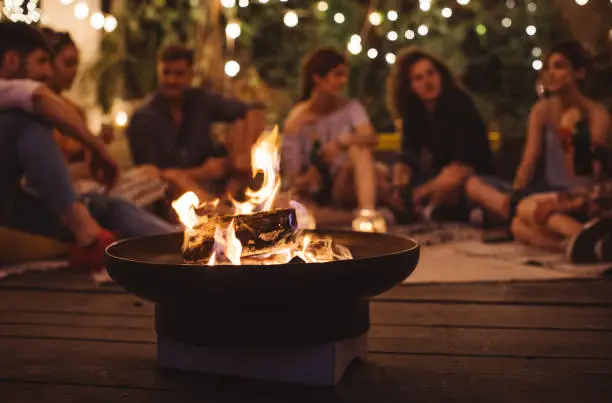 Group of happy young people sitting around fire and having fun.