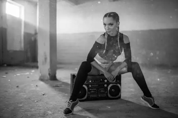 One woman, young dancer, sitting on retro radio, in old warehouse, black and white.