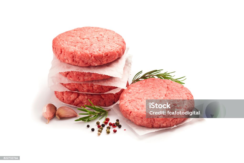 Raw hamburger patties against white background Two raw hamburger patties isolated white background. Predominant colors are red and white. Some cooking and seasoning ingredients like rosemary, garlic, peppercorns and oregano are around the burgers. DSRL studio photo taken with Canon EOS 5D Mk II and Canon EF 100mm f/2.8L Macro IS USM Burger Stock Photo