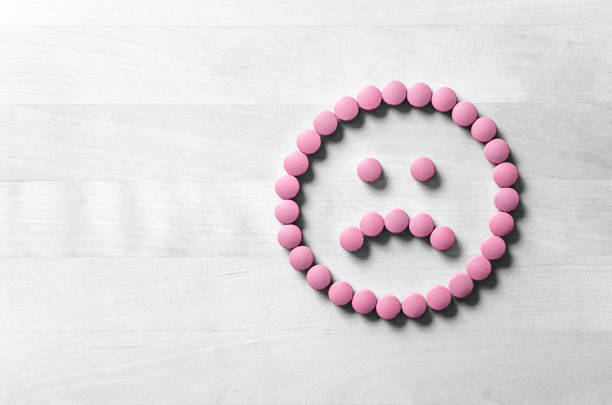 Clinical depression, mental illness and disorder or bad health services concept. Sad smiley face made from pills, medicine and tablets on wooden table. Dissatisfied and unhappy icon. stock photo