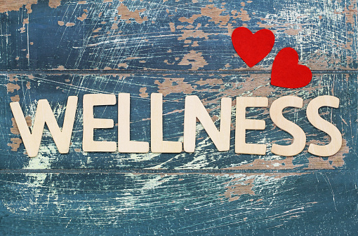 Wellness written with wooden letters on rustic surface and red hearts