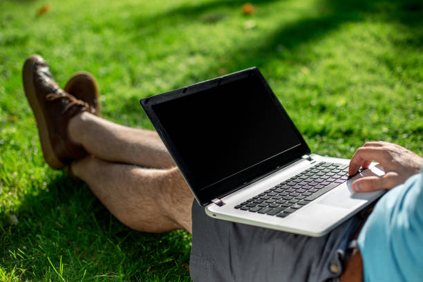 istock Cropped shot of man using laptop with blank screen while sitting on green grass 822867546