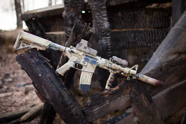 Assault Rifle, painted in sand color on the background of the burnt logs. Airsoft.