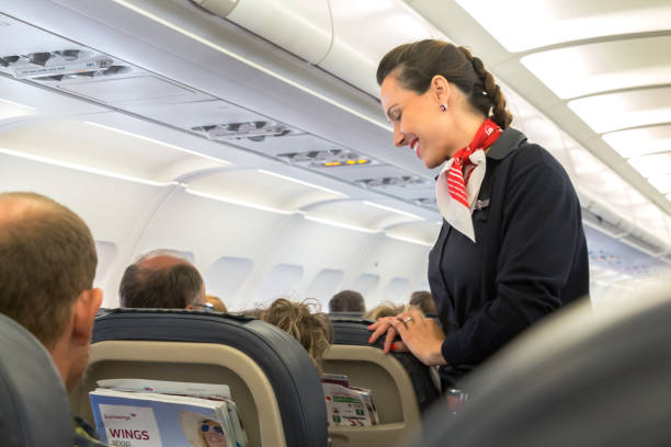 Eurowings flight waiting Thessaloniky: A female flight attendant  is speaking with a passenger sitting in the economy class of the route Thessaloniky - Munich of Eurowings Airline. air stewardess stock pictures, royalty-free photos & images