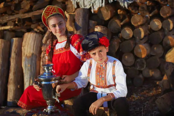 Sister and brother in Russian folk costumes sitting near samovar