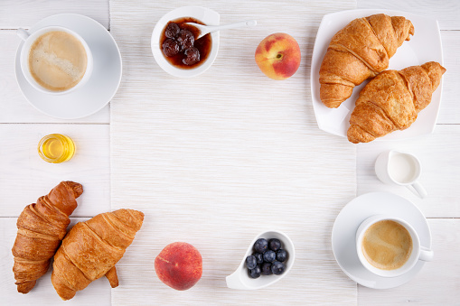 Breakfast - two cups of coffee, croissants, jam, honey and fruits on white table.  Top view. Copy space.