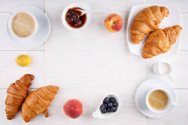 завтрак - две чашки кофе, круассаны, варенье, мед и фрукты на белом столе.  вид сверху. копирование пространства. - croissant morning white breakfast стоковые фото и изображения