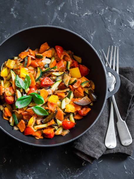 Quick ratatouille in a cast iron skillet on a dark background, top view. Steamed vegetables - vegetarian food concept Quick ratatouille in a cast iron skillet on a dark background, top view. Steamed vegetables - vegetarian food concept ratatouille stock pictures, royalty-free photos & images