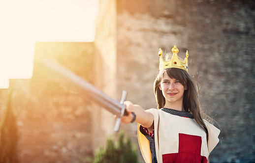Young queen at the castle walls. The queen is holding a sword and is issuing the order to counterattack.\n