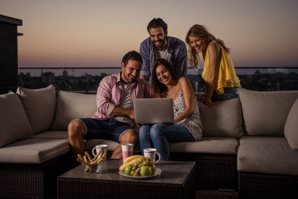istock Smiling couples using laptop together on a penthouse terrace at dusk. 823259844