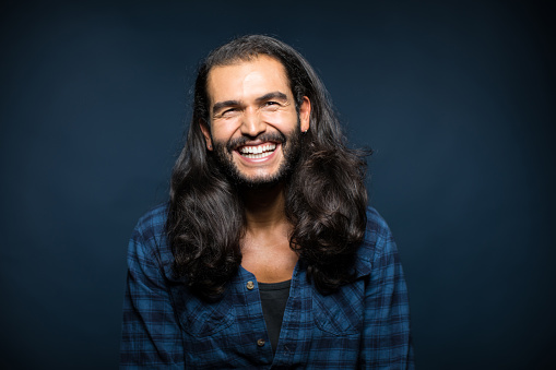 Portrait of cheerful man with long hair. Young male is wearing casuals. He is against blue background.