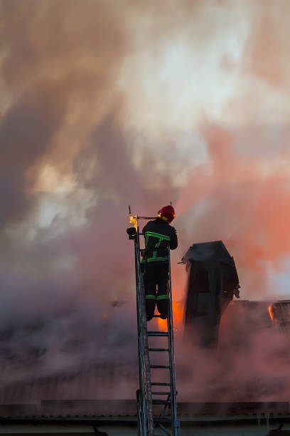 istock Firefighter or fireman on the ladder extinguishes burning fire flame with smoke on the apartment house roof 823311308