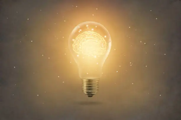 Photo of golden brain glowing inside of light bulb on paper texture background