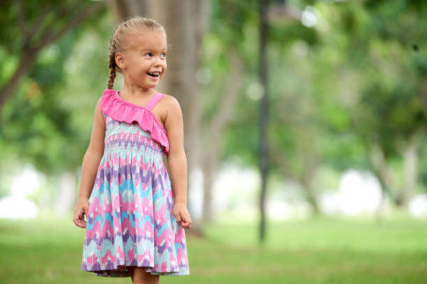 Portrait of happy little girl in summer dress standing in park