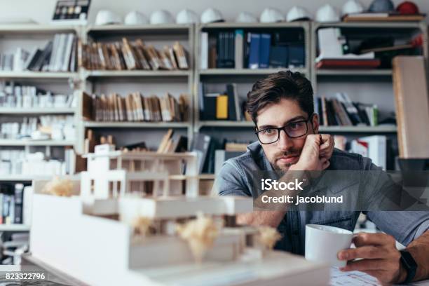Thoughtful Male Designer Looking At Model With Cup Of Coffee Stock Photo - Download Image Now