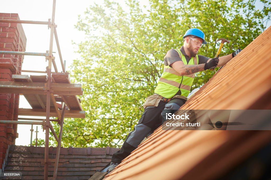 roofer replacing the old tiles a roofer nails on the roof tiles Rooftop Stock Photo