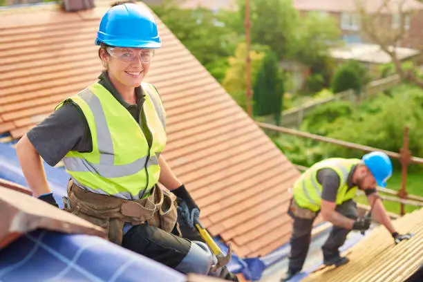 a female roofer nails on the roof tiles with her colleague